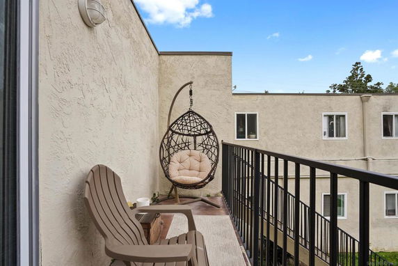 Balcony with chairs and a hanging chair facing neighboring building exteriors.