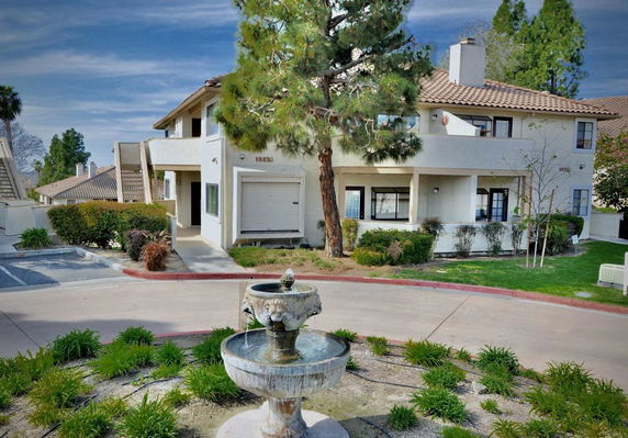 Front view of a two-story building with a tiled roof and a fountain in the foreground.
