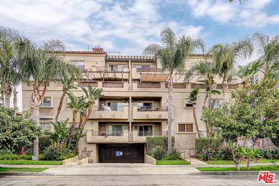 Front view of a multi-story residential building with balconies and palm trees.