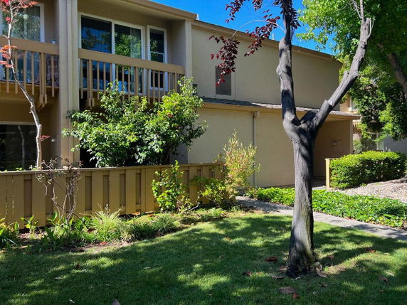 Front view of a two-story house with balconies and surrounding greenery.