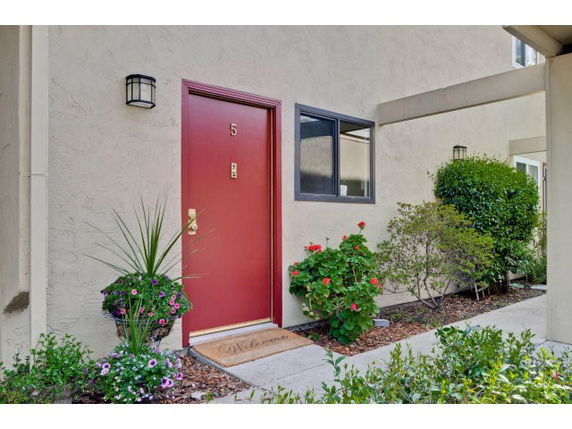 Front elevation of a building with a red door marked number 5 and surrounding plants.