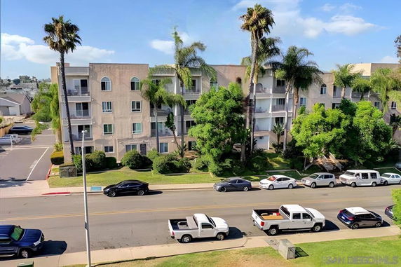 Front view of a multi-story apartment building with balconies and surrounded by tall palm trees.