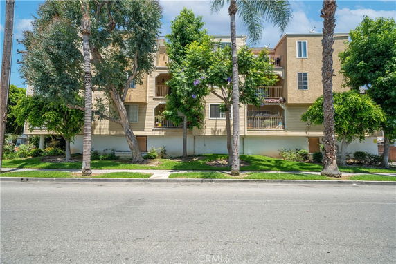 Front view of a multi-story residential building with balconies and trees in front.