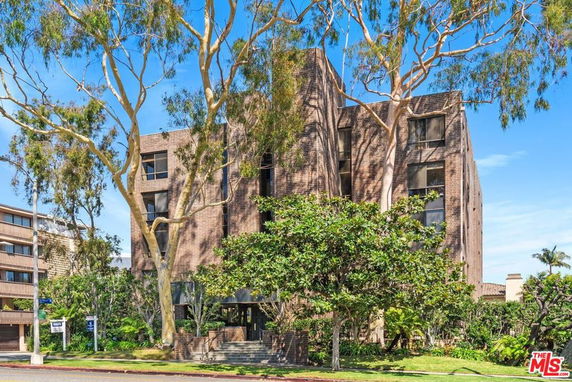 Front view of a multi-story brick building with large trees.