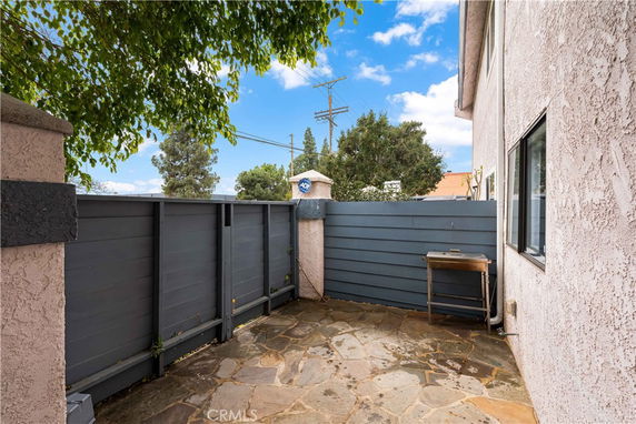 Outdoor area with stone flooring next to a house, enclosed by a tall gray fence.