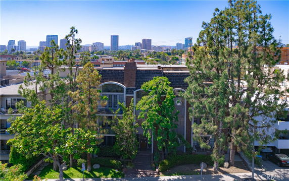 Front view of a multi-story residential building with tall trees in front.