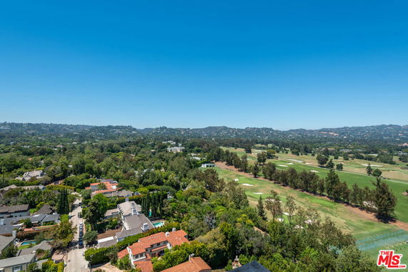 Wide panoramic view of a landscape with houses and a golf course, set against a backdrop of hills under a clear blue sky.