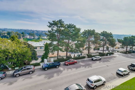 View of residential neighborhood with parked cars and trees along the street.
