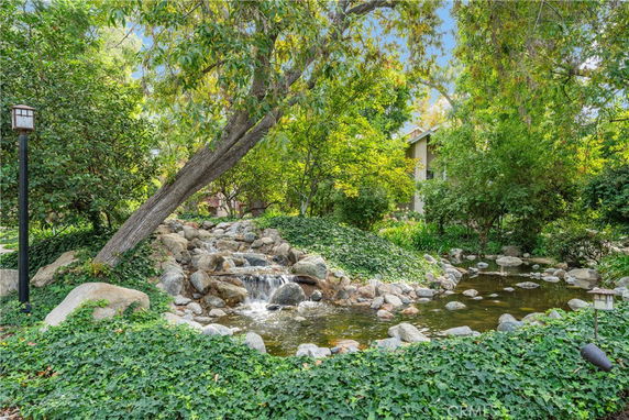 Scenic outdoor view with a small waterfall flowing into a pond surrounded by trees and greenery.