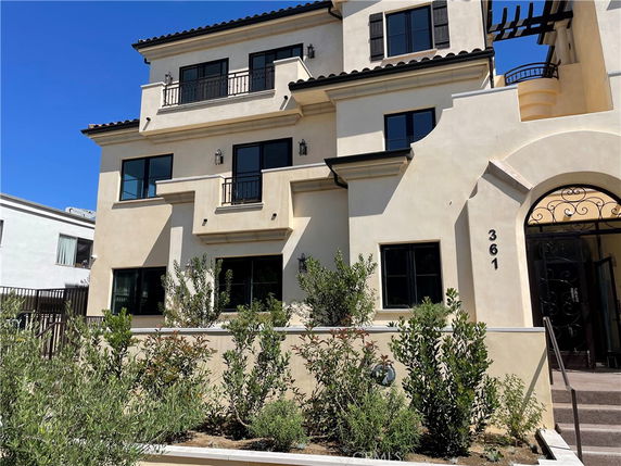 Front view of a multi-story house with balconies and arched entrance.