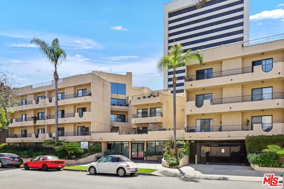 Front view of a multi-story residential building with balconies and palm trees in front.