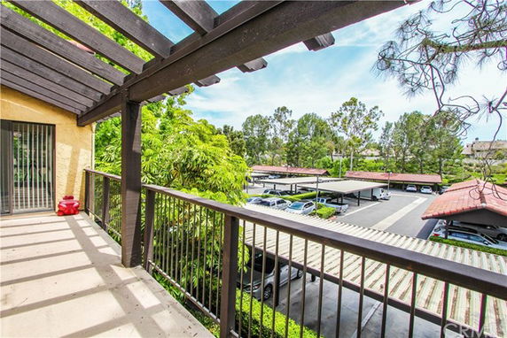 View from a building balcony overlooking a parking area with covered parking spaces.