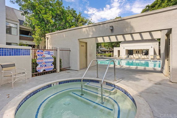 Outdoor swimming pool area with jacuzzi and seating.