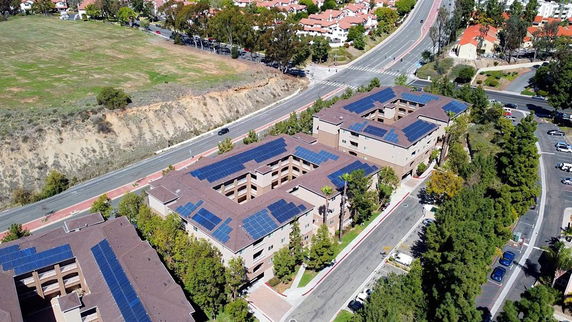 Aerial view of a residential building complex with multiple rooftops equipped with solar panels.