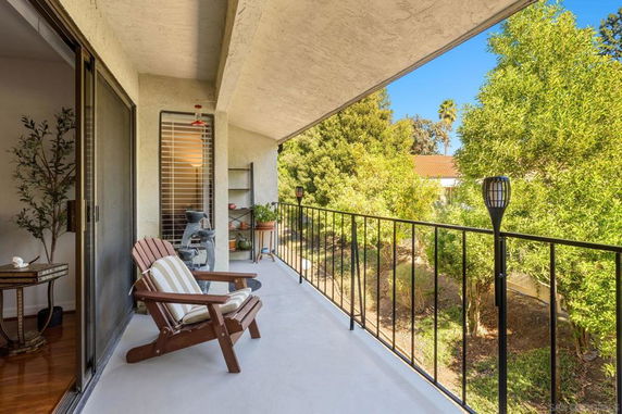 Balcony view with seating and railing overlooking trees and nearby rooftops.