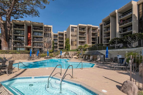Outdoor swimming pool area in front of a multi-story apartment complex.