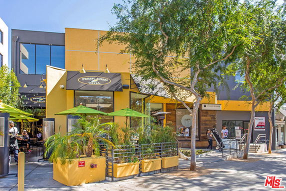 Front view of a modern restaurant building with outdoor seating area and trees.