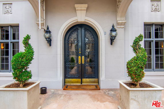 Front view of a building entrance with ornate double doors and decorative plants.