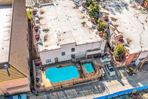 Aerial view of a building complex with a swimming pool and hot tub enclosed by a fence in the courtyard area.