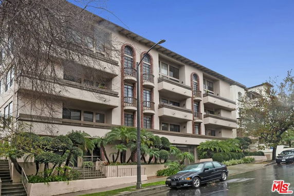 Front view of a multi-story apartment building with balconies and a landscaped entrance.