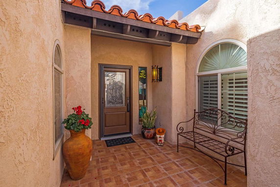 Front entryway of a house with a decorative door, arched windows, and a tiled floor.