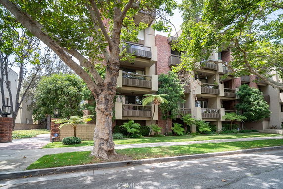 Front view of a multi-story residential building with balconies and trees in front.