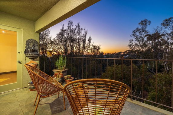 Balcony view with chairs and potted plants overlooking trees and a sunset.