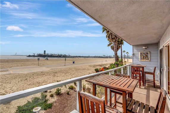 Panoramic view of a beach and ocean from a balcony with wooden furniture.