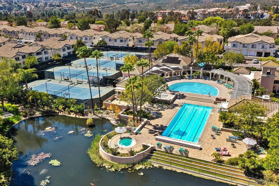Aerial view of a swimming pool area with surrounding ponds and adjacent tennis courts in a residential complex.