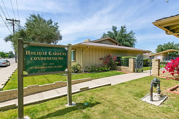 Front view of a single-story condominium building with a sign indicating Holiday Gardens Condominiums.
