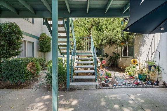 Outdoor view of a building with a staircase leading to an upper level, surrounded by plants and decorative elements.