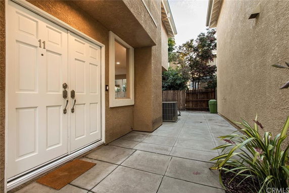 Outdoor entrance area with a double door and adjacent window, surrounded by beige walls.