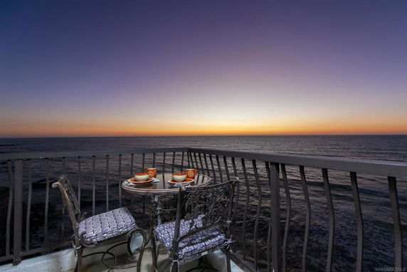 Balcony with ocean view during sunset, featuring a small table and chairs.