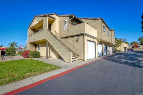 Front view of a two-story building with a staircase leading to the upper level and garages on the ground floor.