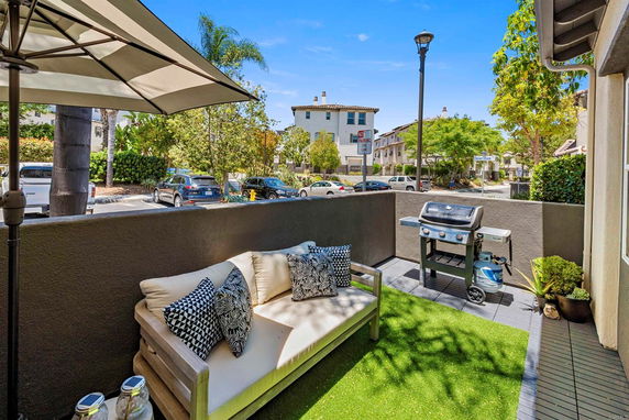 Outdoor patio area with seating and a grill, surrounded by a low wall with a view of neighboring houses and street.