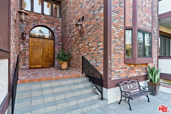 Front view of a brick house with wooden double doors and a staircase.