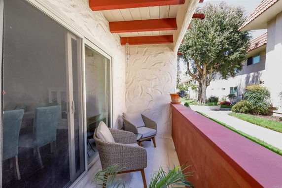 Outdoor area with chairs near a building with sliding glass doors, surrounded by trees and other buildings.