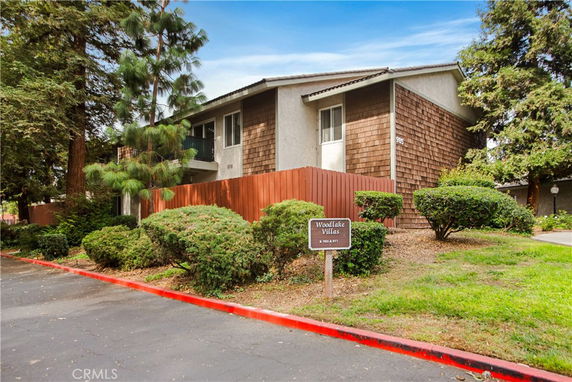 Front view of a residential building with a wooden fence and a sign for 'Woodlake Villas'.