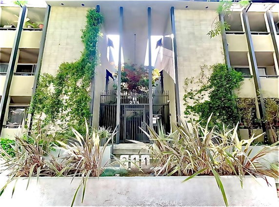Front view of a multi-story building with plants and a gated entrance.