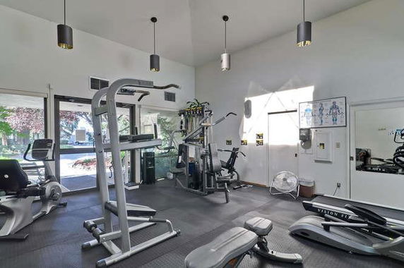 Interior view of a gym area with various exercise equipment and large windows.