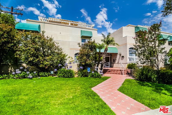 Front view of a building with green awnings and a landscaped garden.