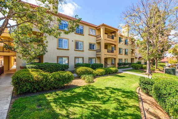 Front view of a three-story apartment building with balconies and a landscaped garden.