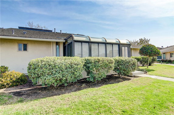 Front view of a house with a sunroom and trimmed bushes.