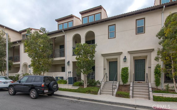 Front view of a multi-story residential building with balconies and stairs leading to the entrances.