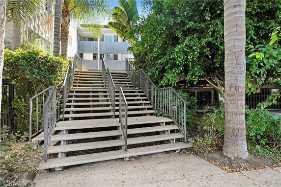 Front view of a multi-story building with staircase and greenery.