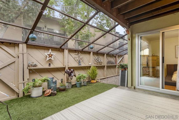 Patio with artificial grass, potted plants, and a sliding glass door leading inside.