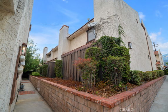 Side view of a two-story stucco house with a brick-bordered garden area.