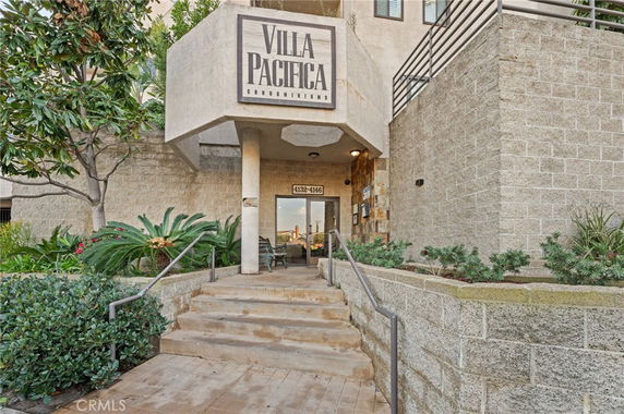 Front view of a condominium entrance with stairs leading up to the door and a sign reading 'Villa Pacifica'.