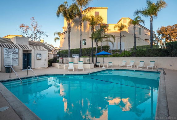 Outdoor swimming pool area with lounge chairs and surrounding building in the background.