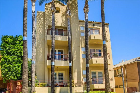 Front view of a multi-story building with balconies and palm trees.